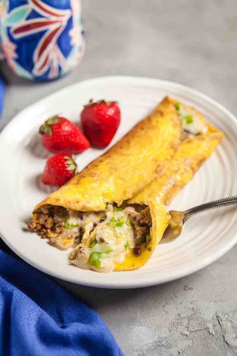 Mexican omelette with chorizo and bell peppers on a plate. A firm is taking a bit out of it and there are strawberries in the background. 