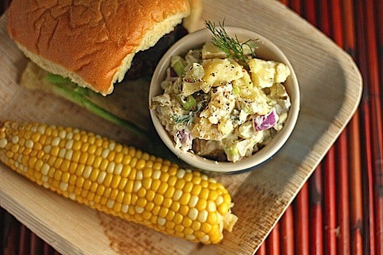 A picnic plate with a burger, corn on the cob, and hummus potato salad made without mayonaisse. 