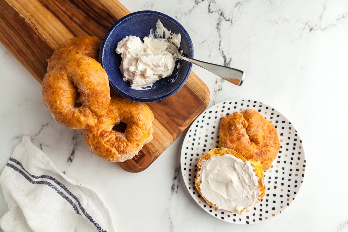 Landscape image of a breakfast table with a plate with an air fryer pumpkin bagel and more bagels to the side. 