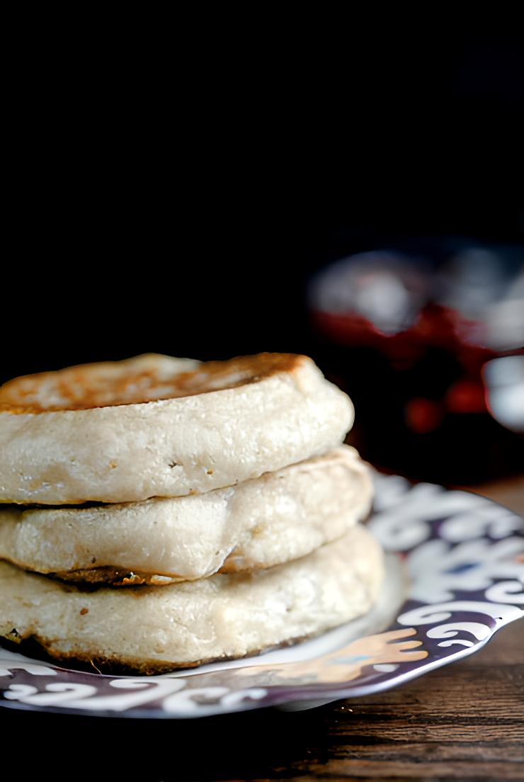 A stack of fluffy homemade crumpets on a small plate against a dark background. 