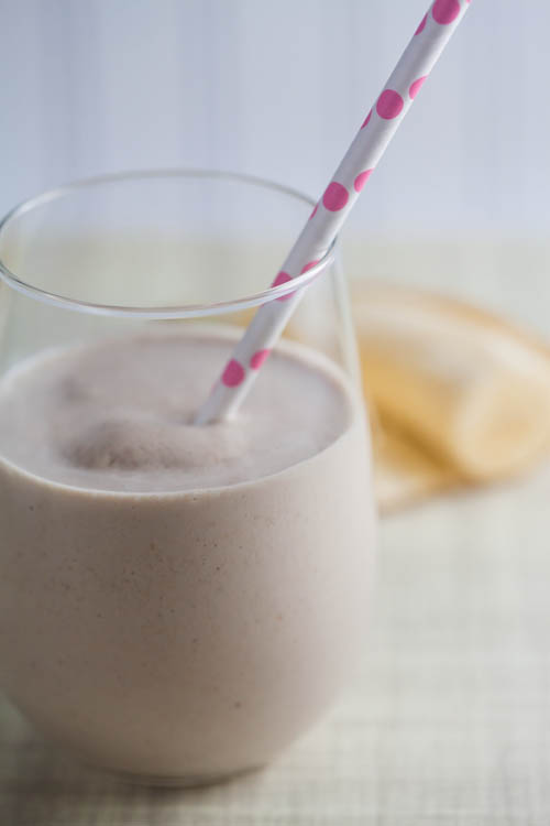 A creamy oatmeal smoothie in a glass, with a pink straw. 