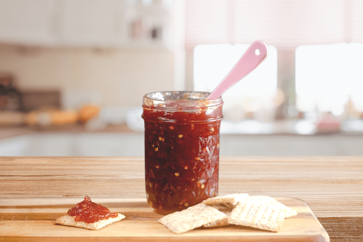 small jar of tomato jam on a wooden counter.