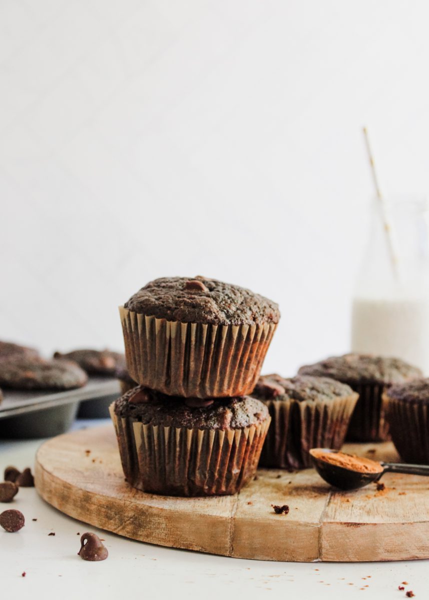stacked chocolate muffins on a wooden board, with milk in the background.