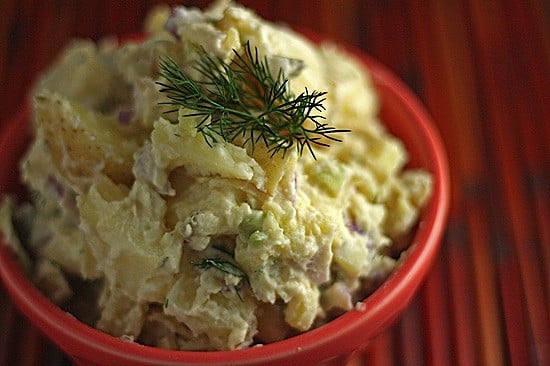 Close up image of mayo free potato salad made with hummus and yogurt on a red bamboo background. 