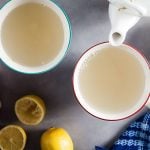 holding a mug of ginger lemon tea with a blue blanket and a teapot