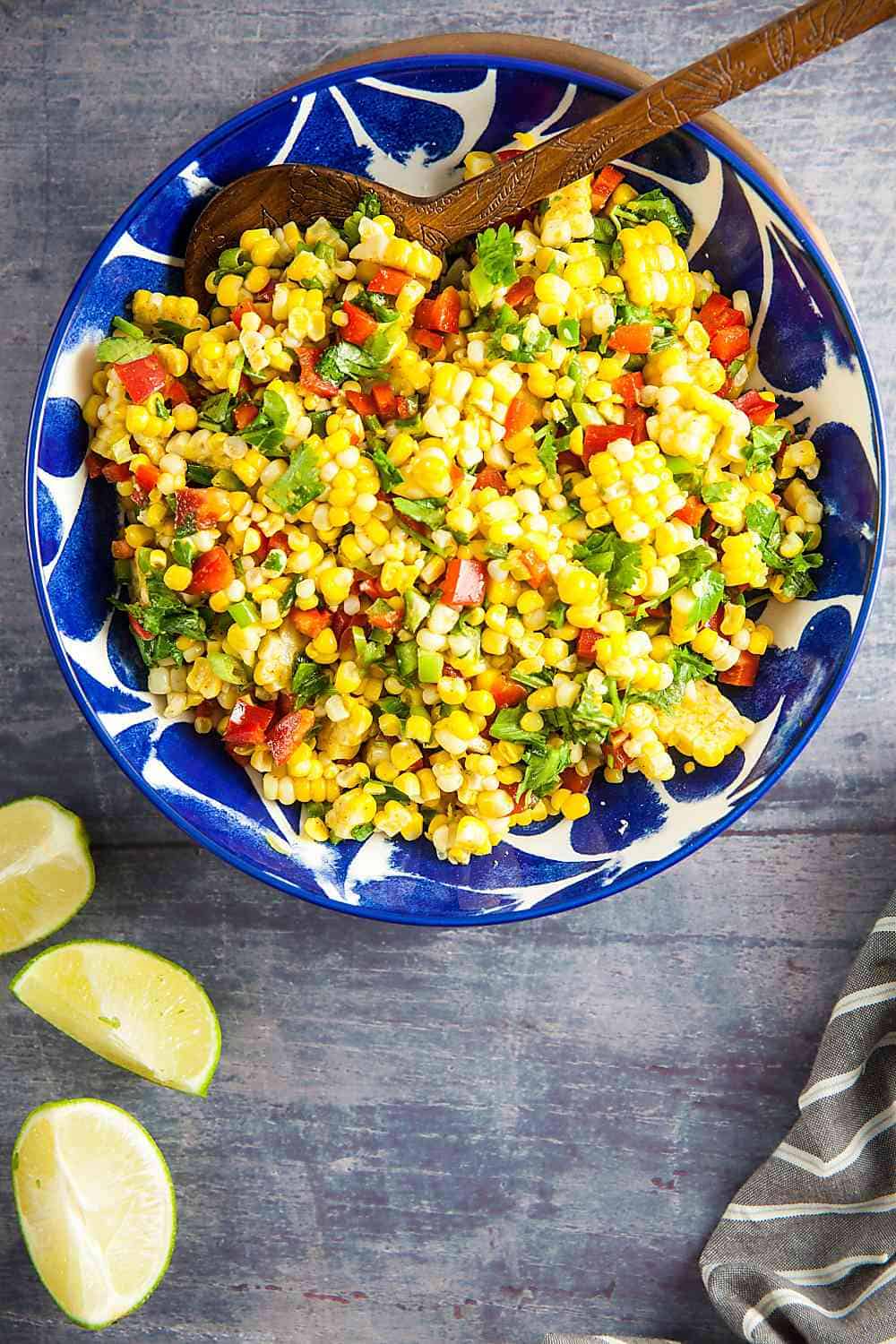 blue bowl of corn salad with three limes