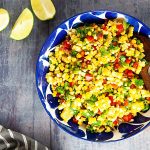 curried corn salad in a blue bowl with limes