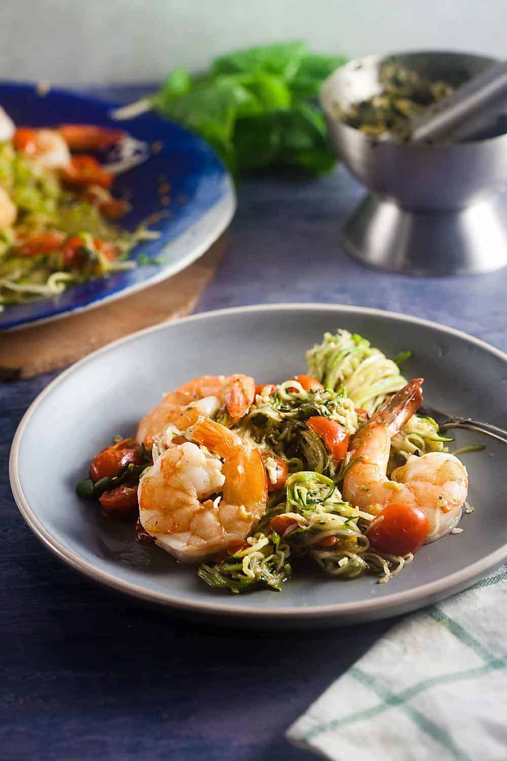 pesto zucchini noodles with baked shrimp on a dinner plate