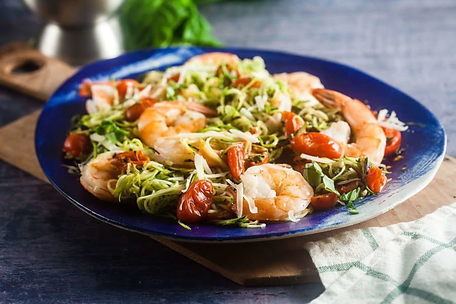 pesto zucchini noodles with baked shrimp on a blue platter