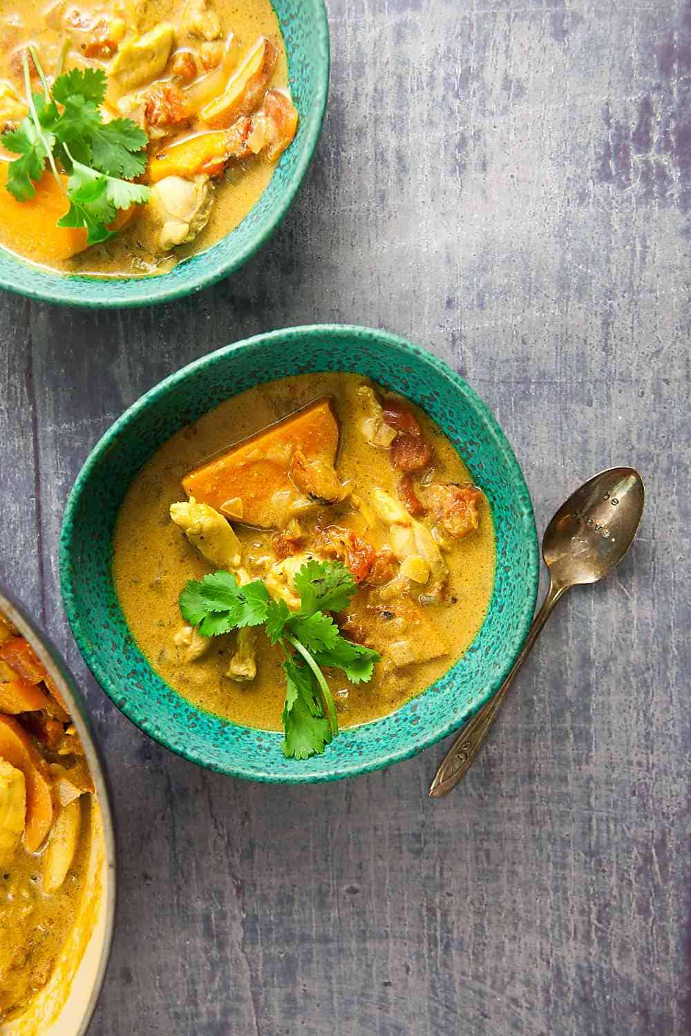 three green bowls filled with chicken sweet potato soup and a spoon on a grey background