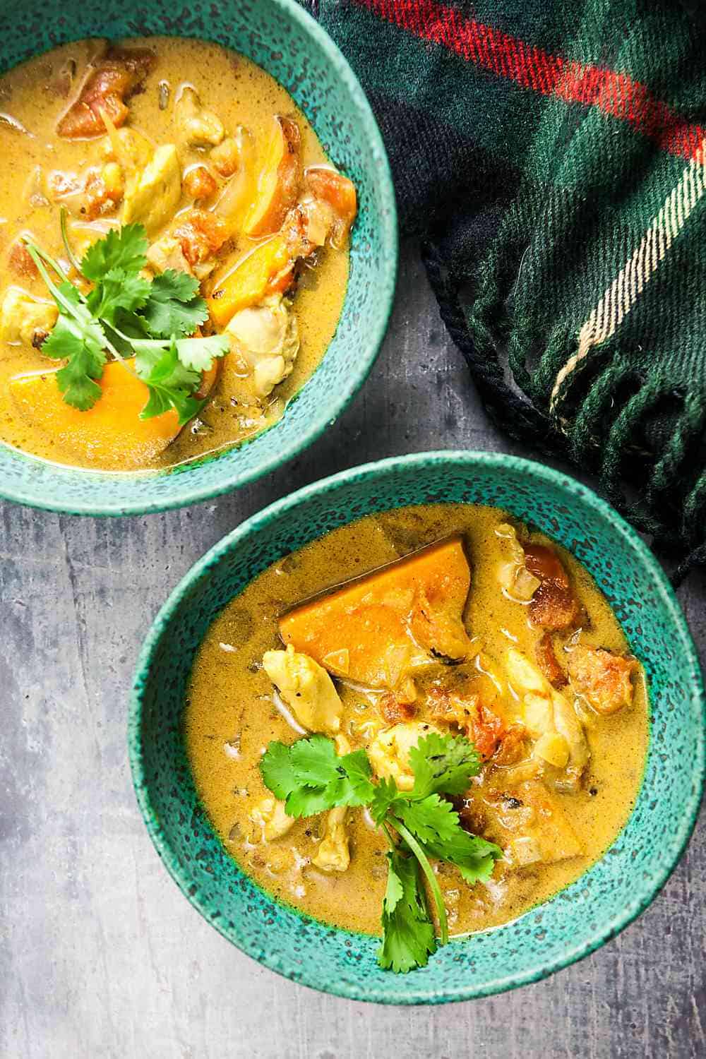 a closeup of two green bowls filled with chicken sweet potato soup on a grey backgrouns with a green plaid blanket