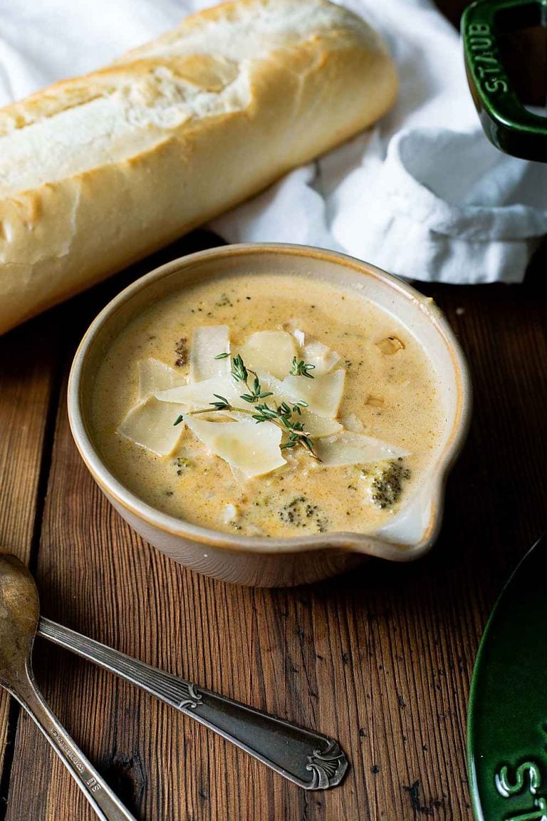 bowl of broccoli cheese soup on a brown table with baguette
