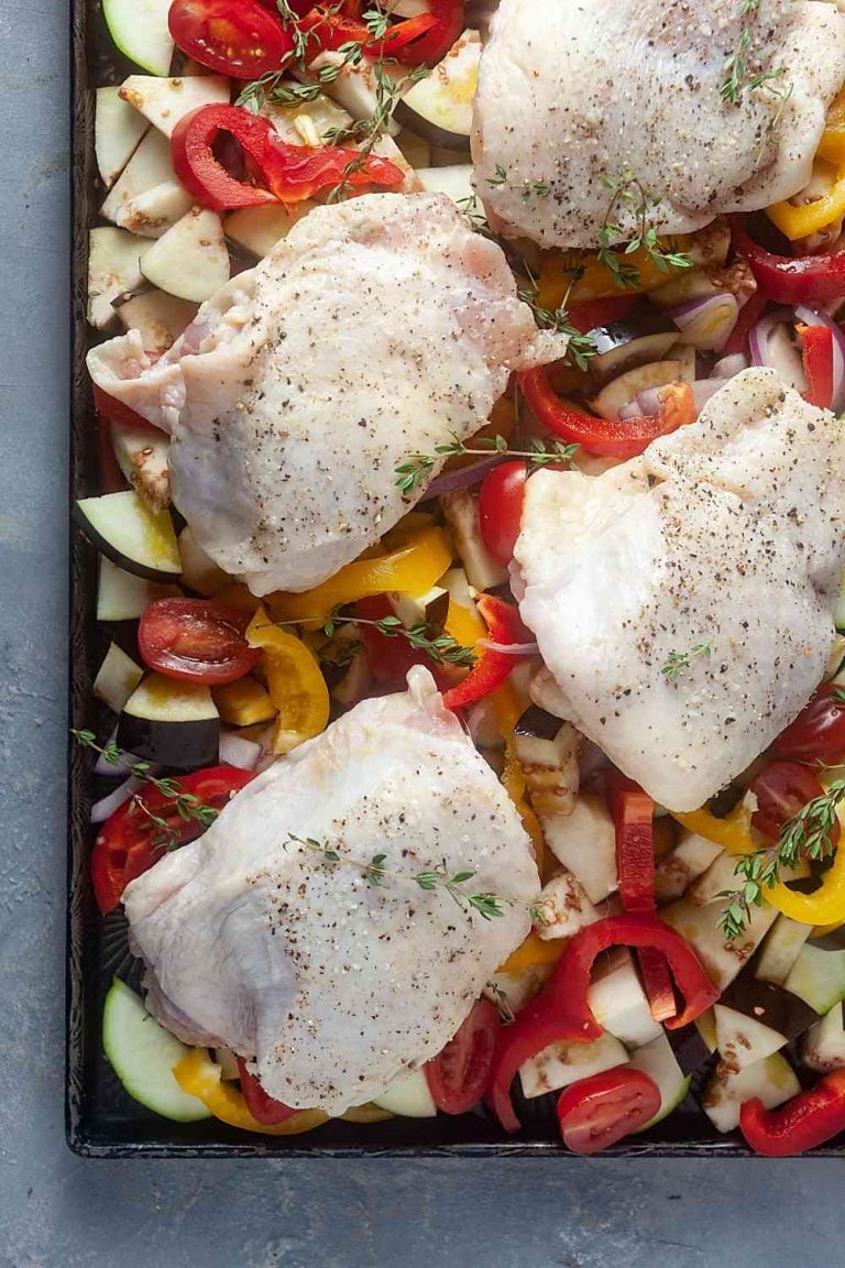 vegetables and chicken thighs on a sheet pan, ready to go into the oven