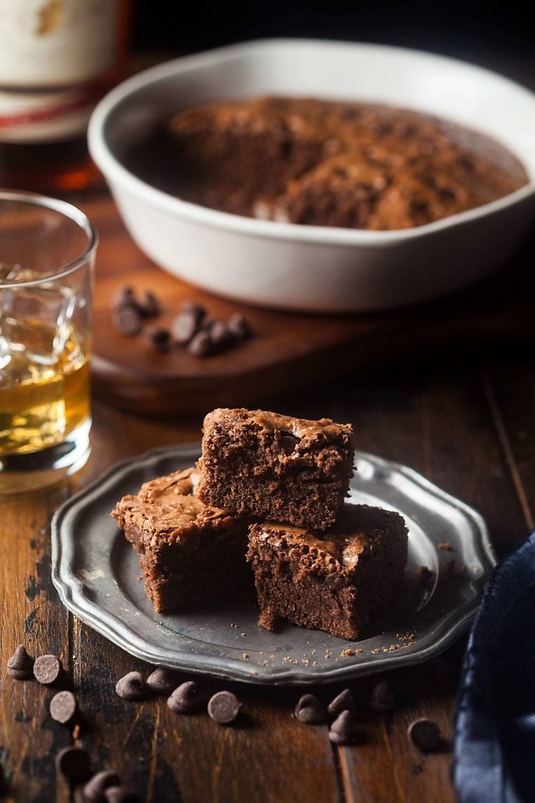 a plate of Irish whiskey brownies with a glass of whiskey and a pan of brownies behind