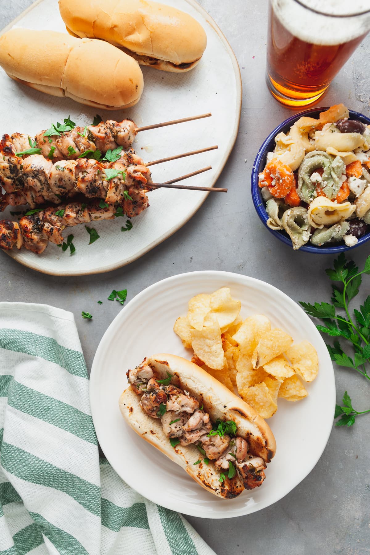 Overhead view of homemade chicken spiedies with pasta salad and a beer. 