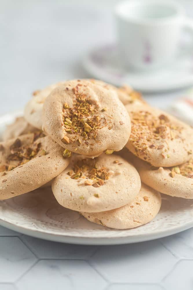 a pile of pistachio meringue cookies on a plate with an espresso cut in the background