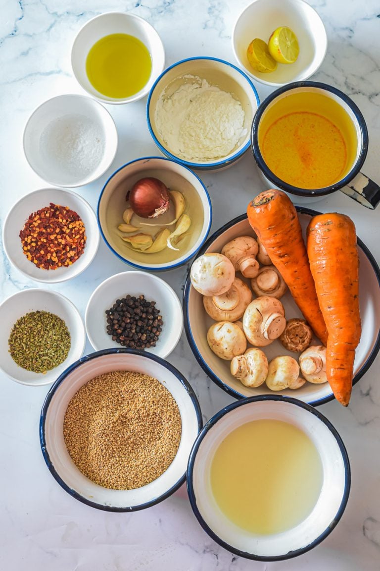 an overhead view of the ingredients needed to make mushroom and quinoa soup, include mushrooms,  quinoa, carrots, coconut milk, broth, fresh herbs, and spices