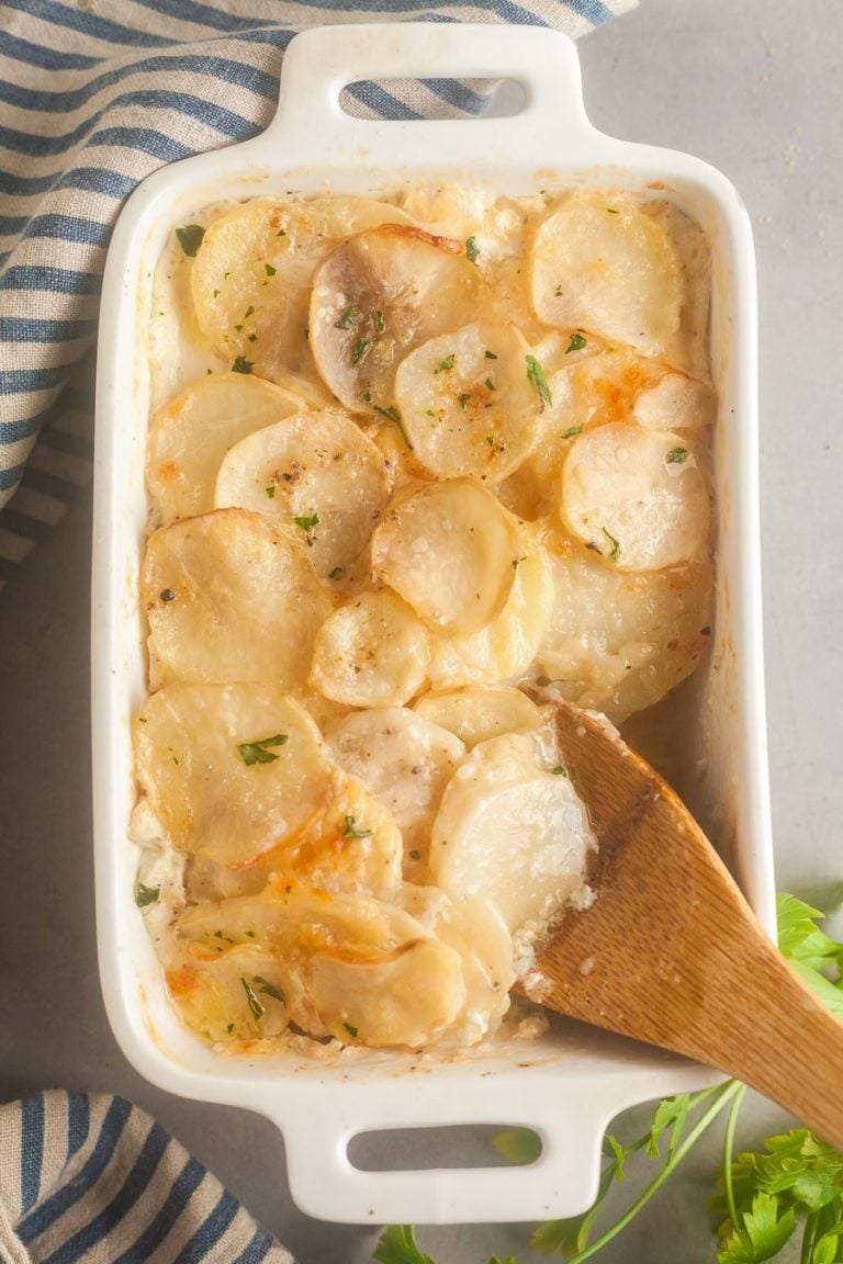 Taking a scoop out of a pan of cheesy scalloped potatoes. 