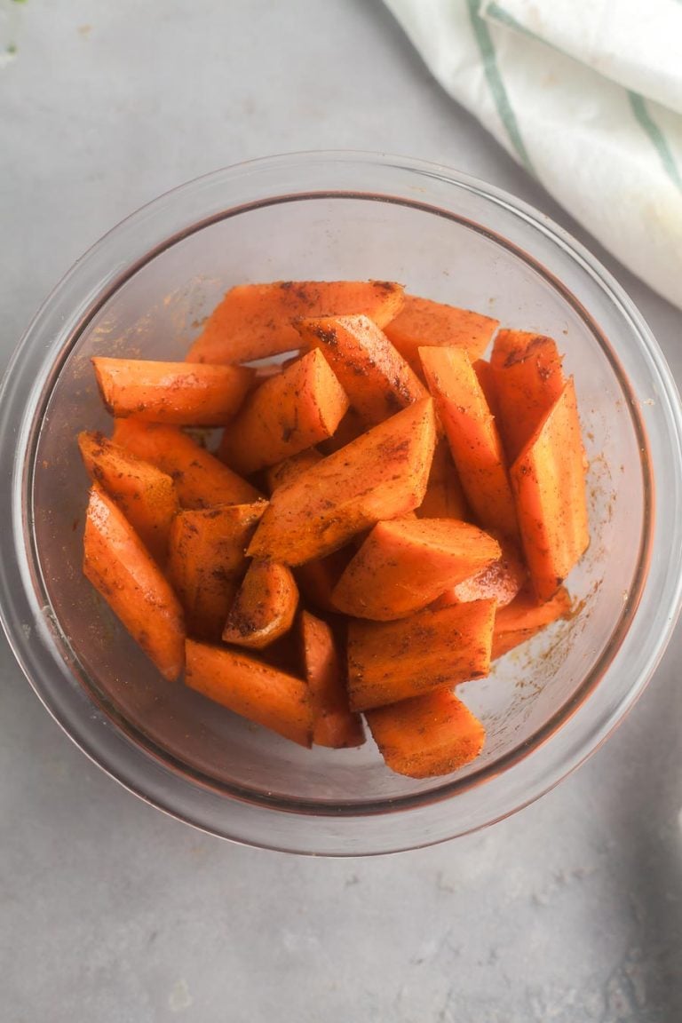A mixing bowl full of carrots drizzled with olive oil and warm Moroccan spices, reach to be roasted