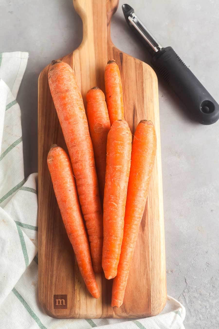 Carrots on a cutting board, ready to be peeled.