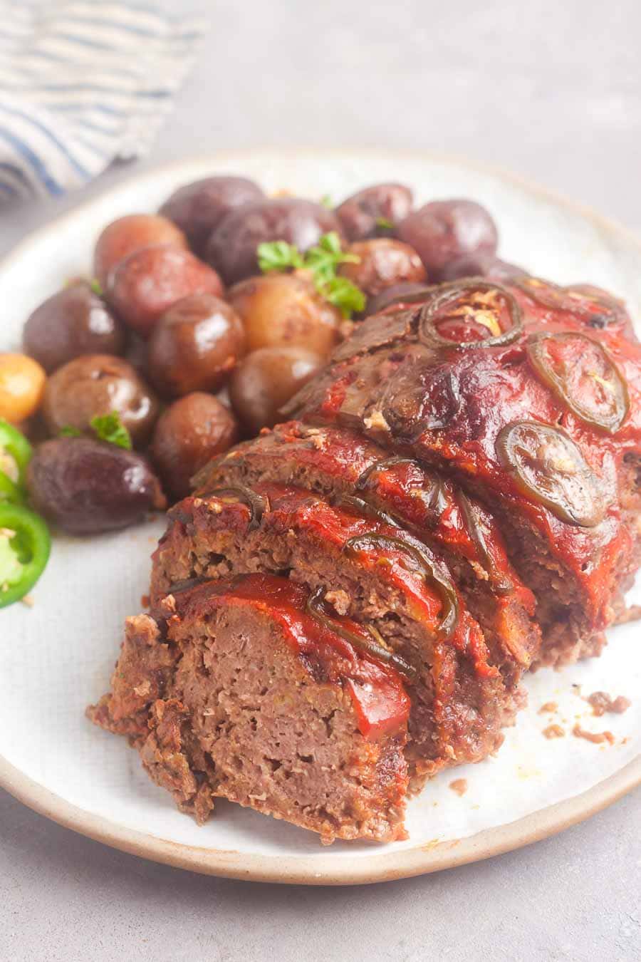 a partially sliced crockpot meatloaf on a serving plate, with potatoes in the background