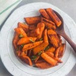 A bowl of Moroccan roasted carrots with a serving spoon.