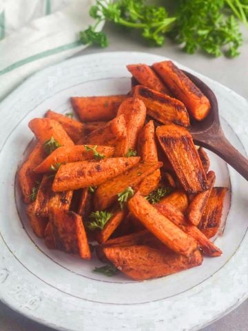 A serving bowl of roasted carrots with Moroccan spices and fresh parsley.