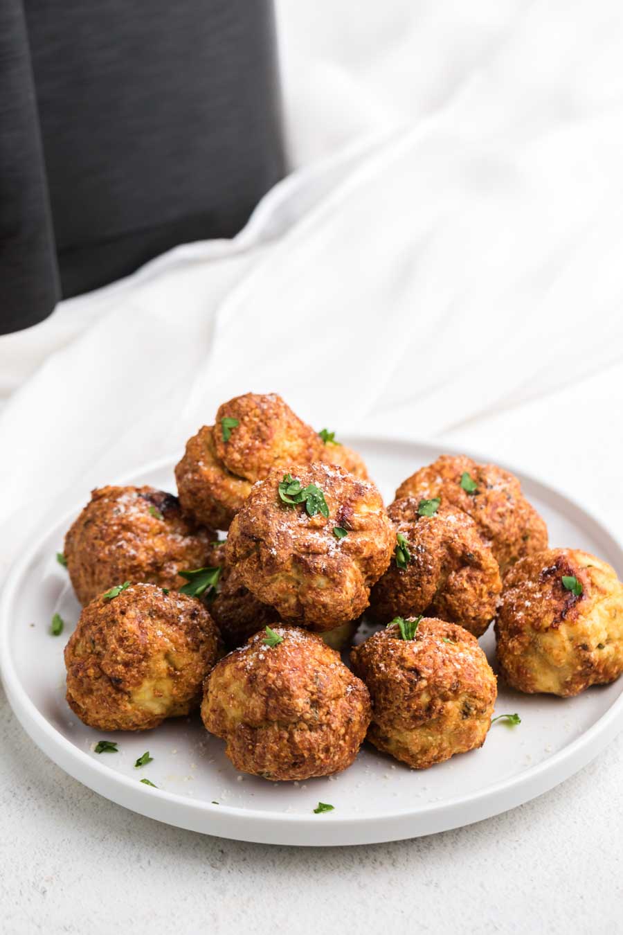 A white plate piled high with chicken meatballs and an air fryer in the background. 