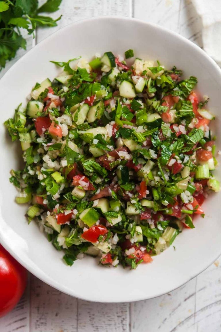 A close up, overhead view of tabbouleh salad with cauliflower rice, tomatoes, cucumbers, and fresh herbs. 