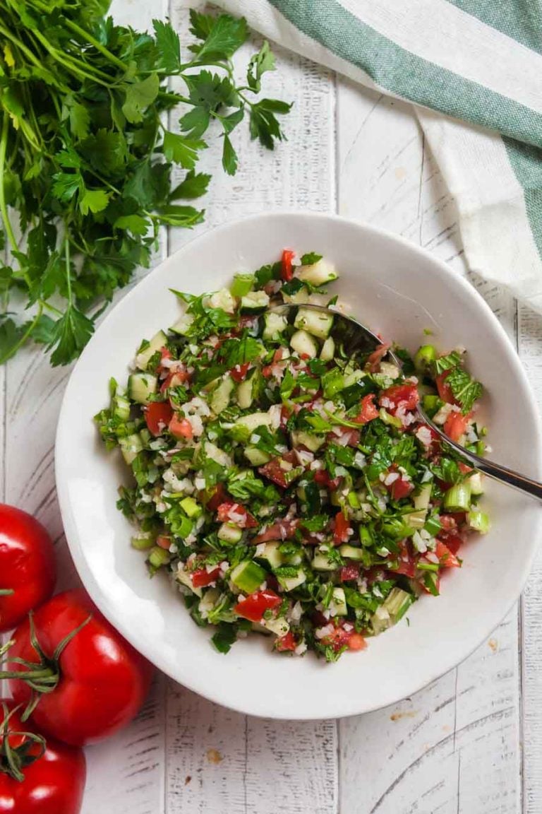 Overhead view of a white serving bowl of cauliflower tabbouleh on a white background. 