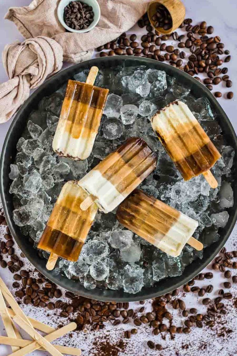 An overhead view of an ice-filled platter layered with low-carb popsicles. Coffee beans and coffee grounds scattered on the background.  