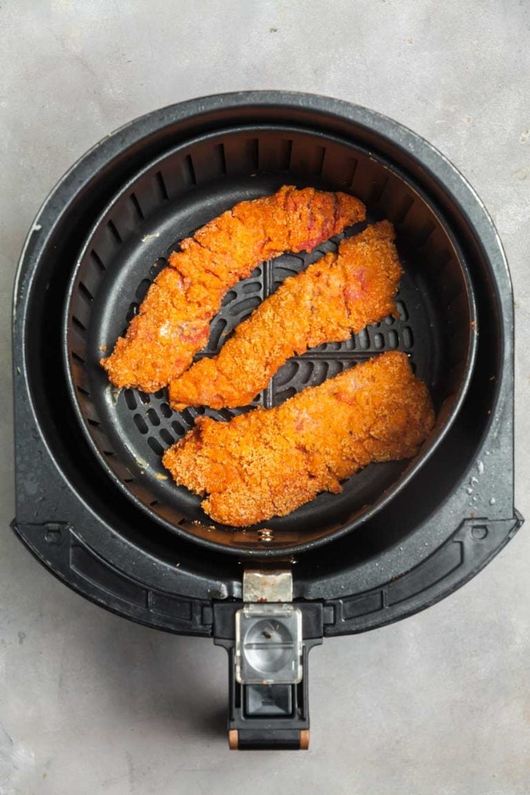 an overhead view of an air fryer backer with three Nashville hot steak fingers inside, ready to be cooked. 