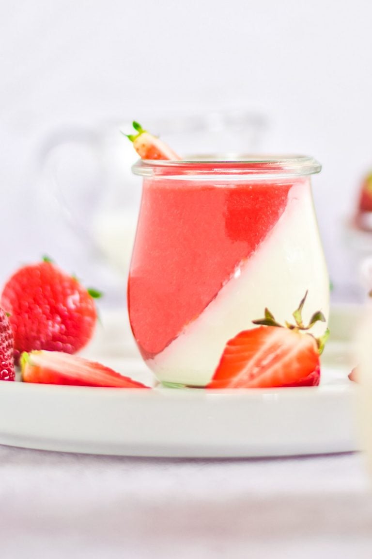 A single serving of vegan panna cotta in a jar layered with strawberry sauce. 