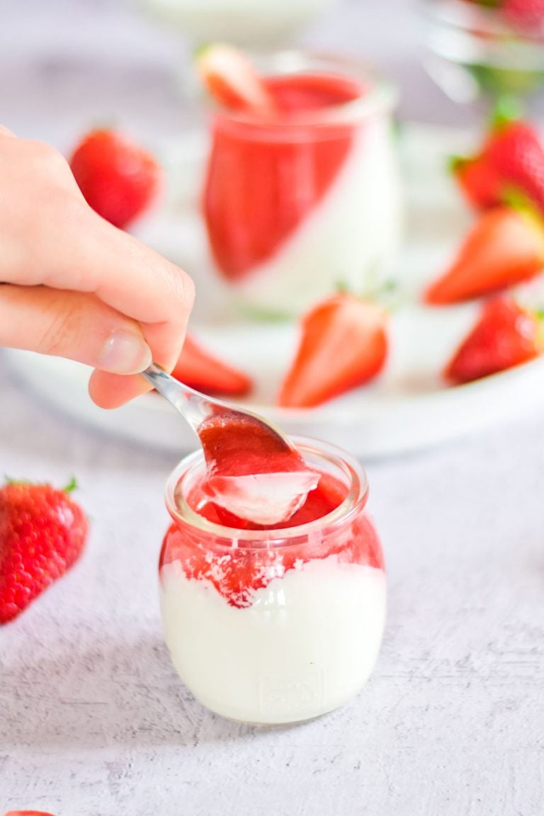 a spoon digging into an individual jar of vegan strawberry panna cotta to show the texture of the two layers