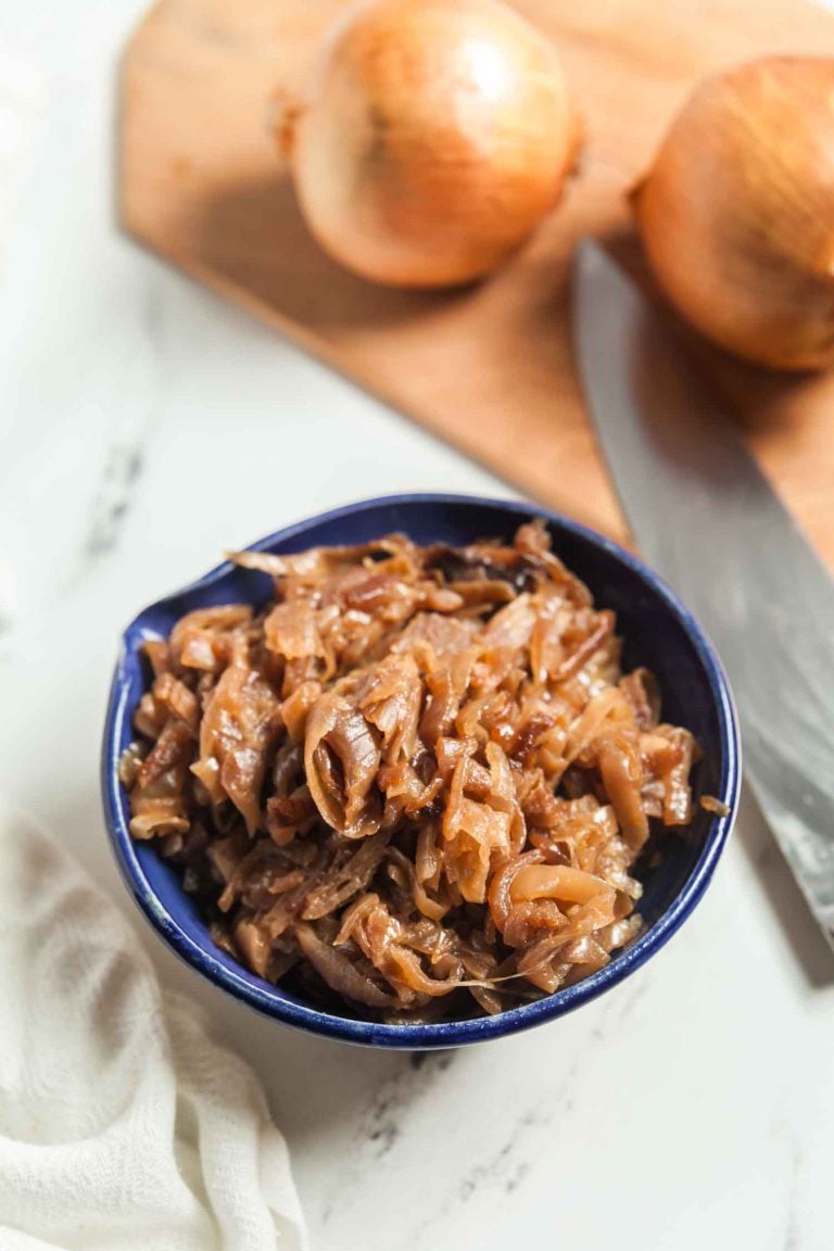 A small blue bowl filled with slow cooker caramelized onions on a white marble background. 