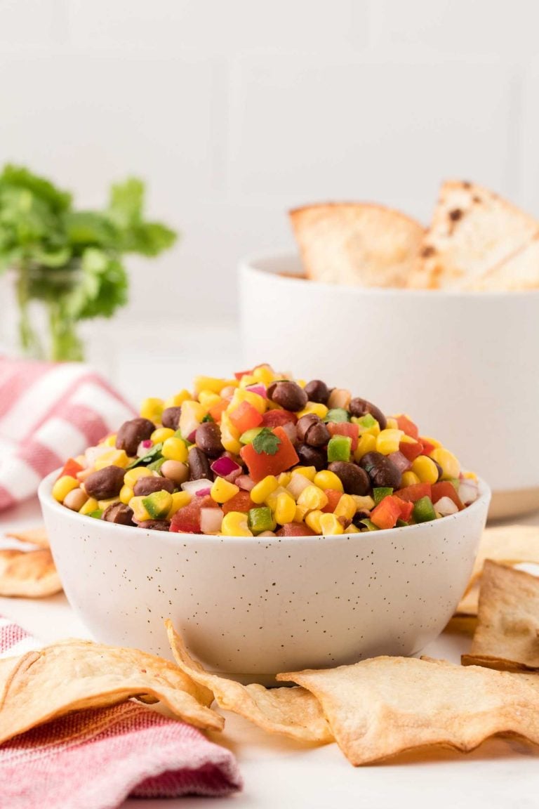 Side view of a bowl filled with vibrant cowboy caviar, surrounded by homemade tortilla chips. 