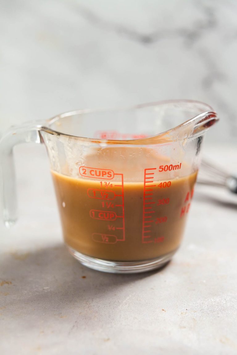 A measuring cup filled with golden brown mushroom gravy.