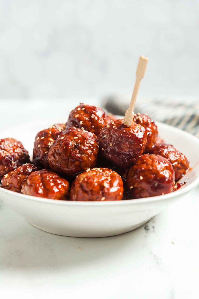A white serving bowl filled with cranberry meatballs appetizers and a cocktail pick for serving them. 