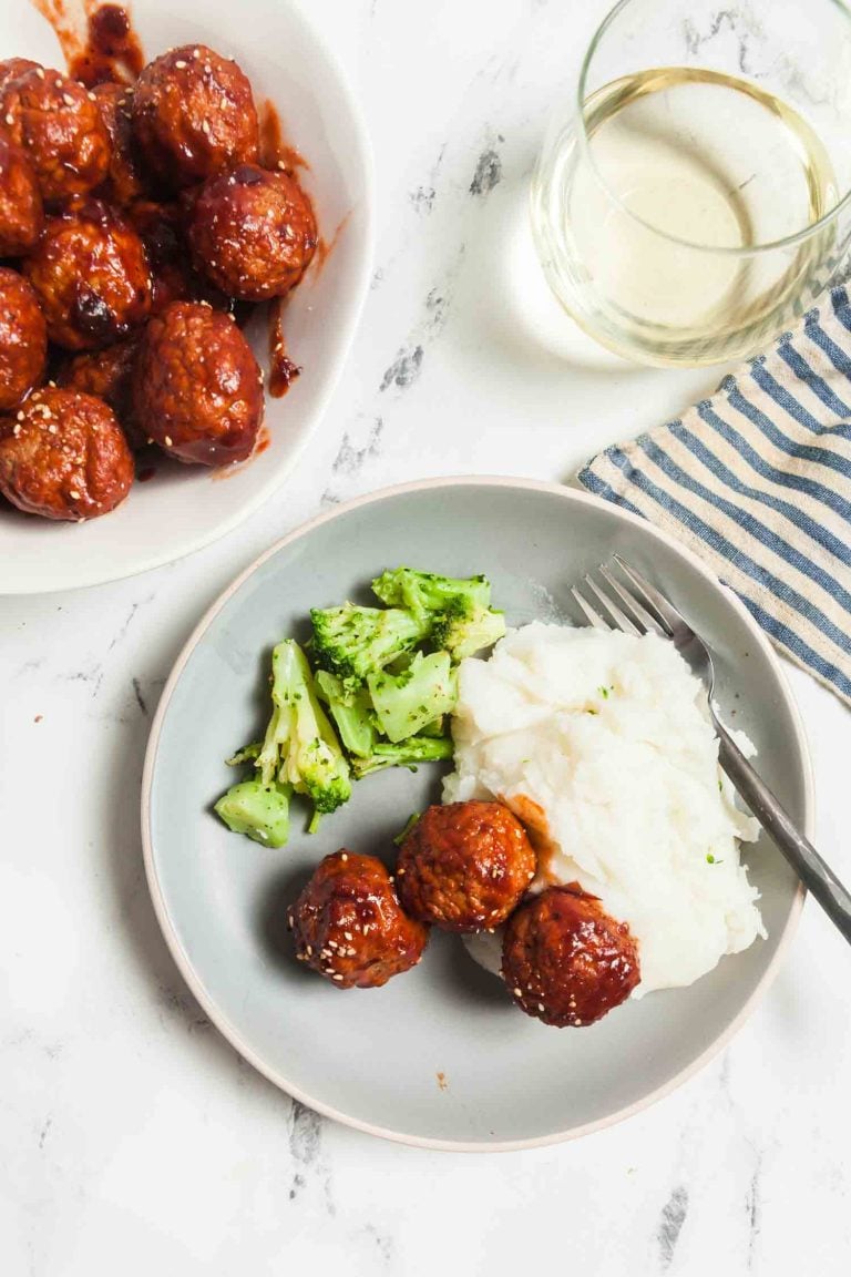 Overhead view of a light grey plate with cranberry glazed meatballs, mashed potatoes, and broccoli. 
