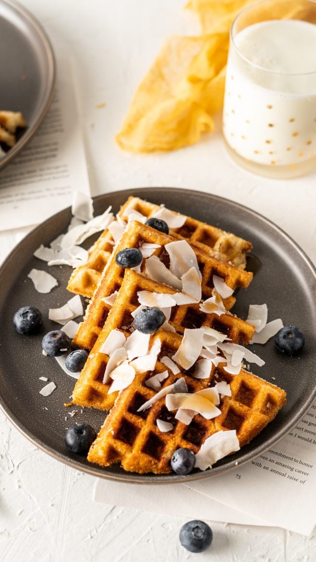 A black plate with a keto waffle topped with berries and coconut. 