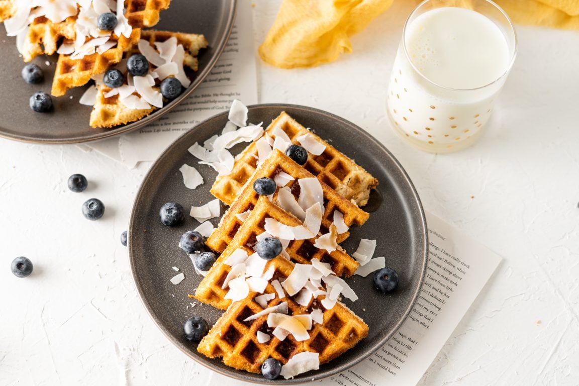 Landscape image of a keto waffle plated with berries and coconut. 