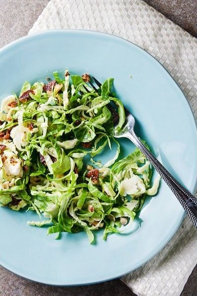 A blue plate with shaved Brussels sprout salad and a fork. 