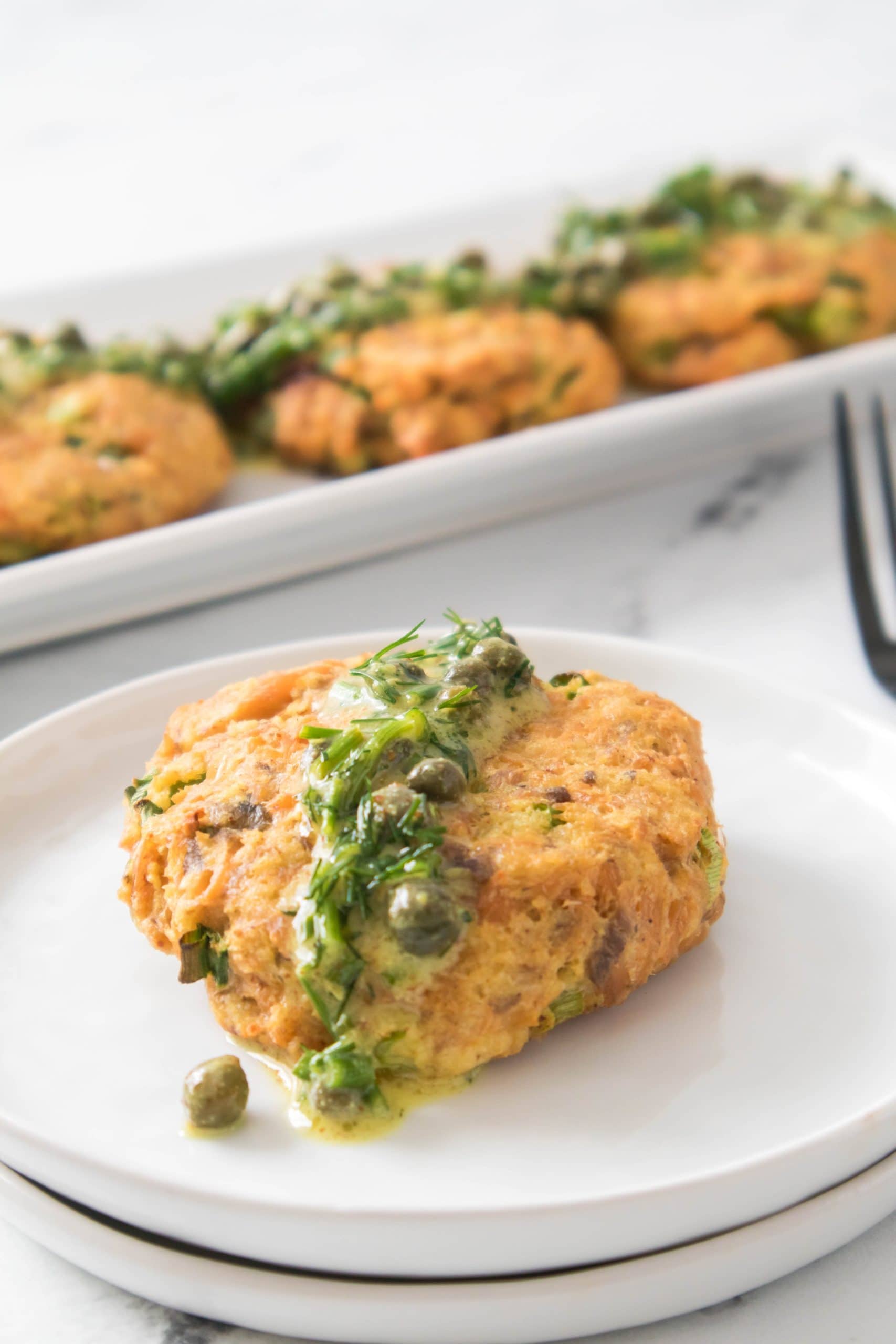 Old fashioned salmon patty with herb sauce on a white plate. 