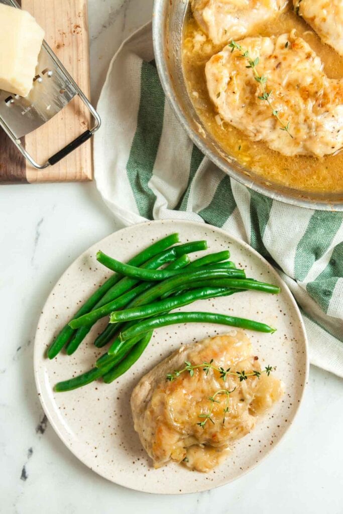 Overhead view of a plate of skillet French onion chicken breasts smothered with gruyere cheese and served with steamed green beans. 