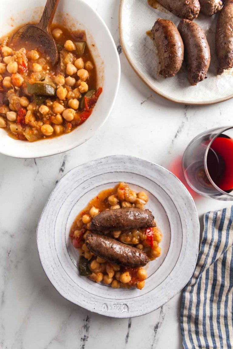 Two beef sausages on top of eggplant and chickpea stew.