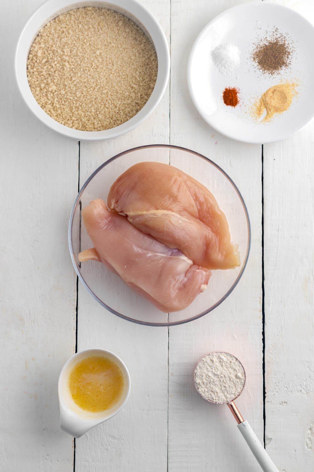 Overhead image of ingredients needed to make chicken nuggets in the air fryer, including chicken breasts, butter, panko bread crumbs, and seasonings. 
