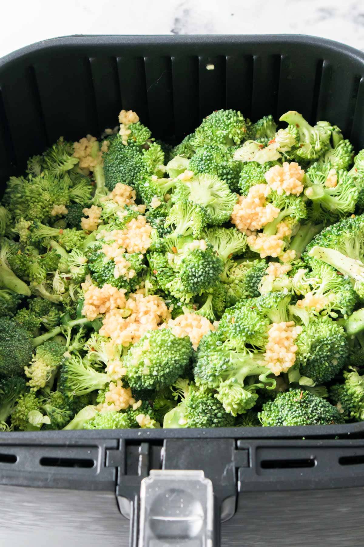 The air fryer basket with broccoli and garlic scattered over the top. 
