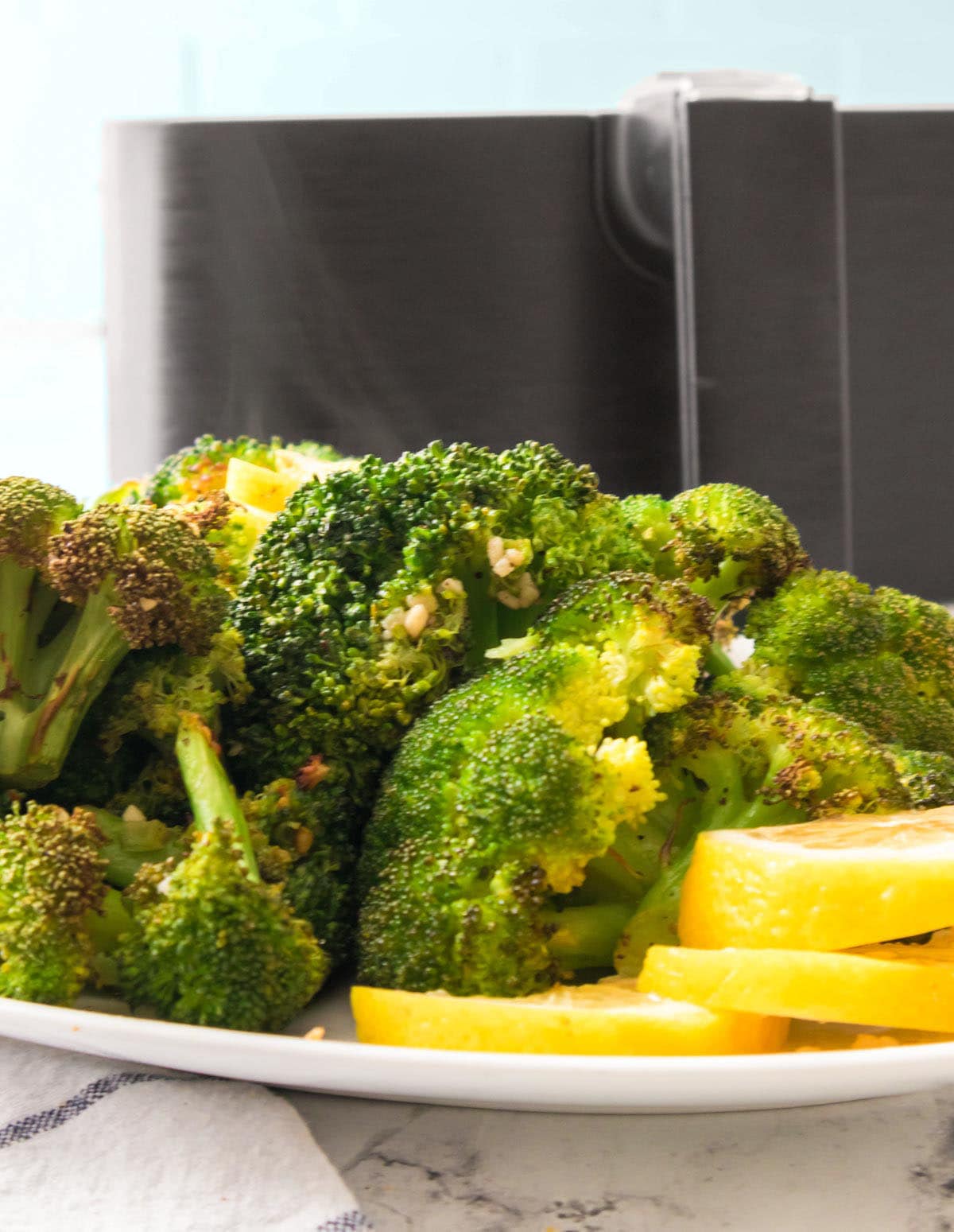 A platter of crispy air fried broccoli in front of the air fryer basket. 