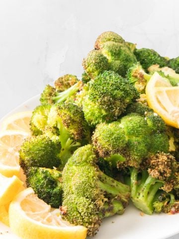 A serving platter of crispy air fryer broccoli with lemon wedges.