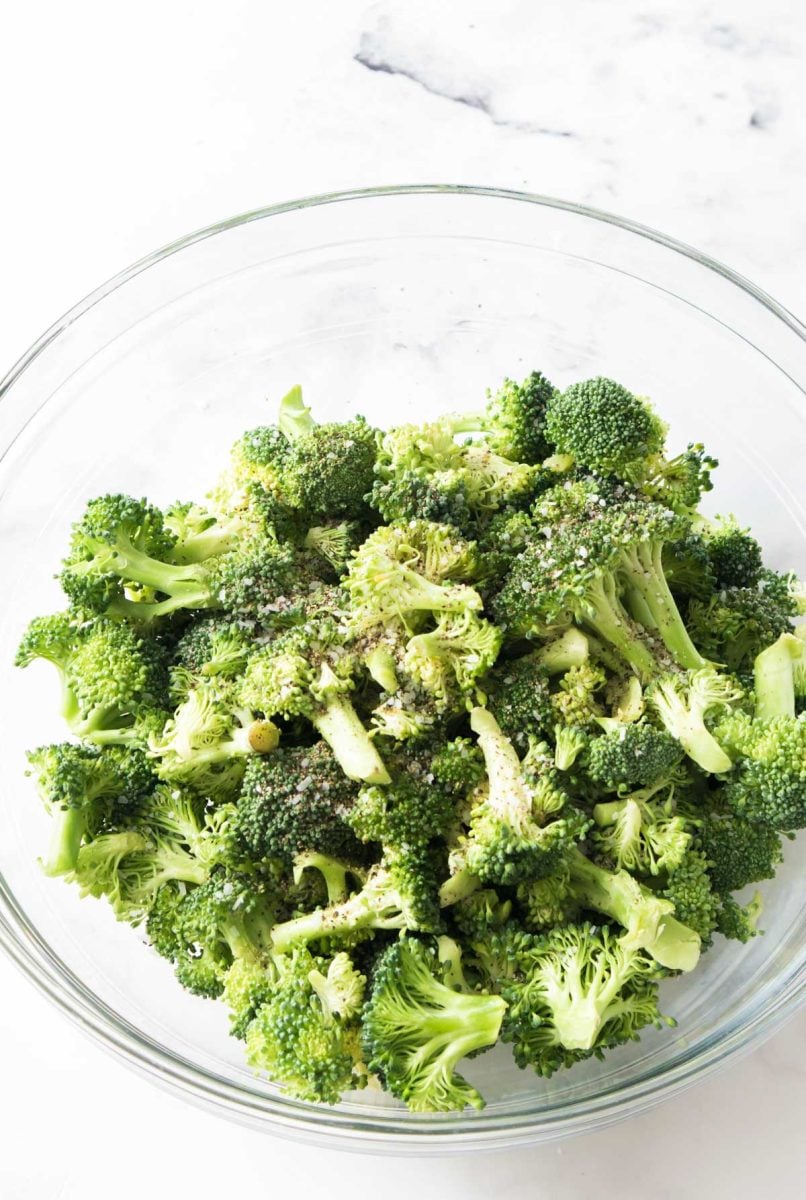 A mixing bowl of seasoned broccoli, ready to go in the air fryer.